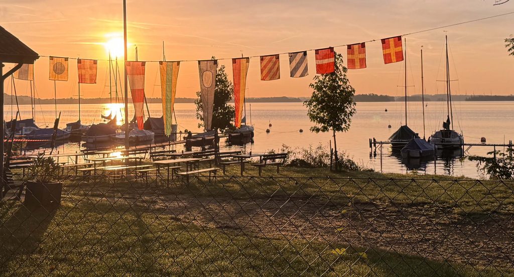 Absegeln 2025 am 20. September 2025. Sonnenaufgang über dem Plöner See. Im Vordergrund das festlich geschmückte Vereinsgelände der Ascheberger Seglergemeinschaft.
